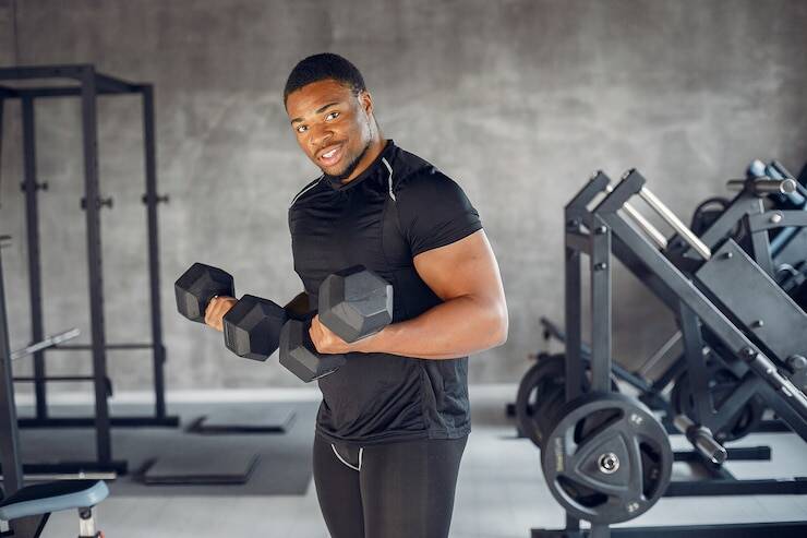 Happy Black man in gym lifting dumbbells, showing how fitness boosts happiness and self-esteem for men