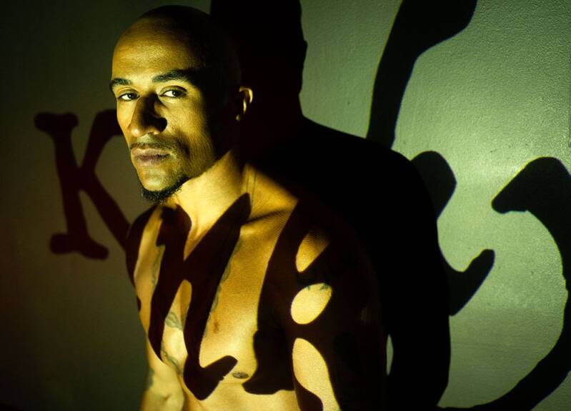 Shirtless Black man with shaved head and goatee, intense gaze, stark lighting casting bold gothic shadows—symbolizing shadow masculinity, men’s mental health, and the dynamic interplay of light and dark.