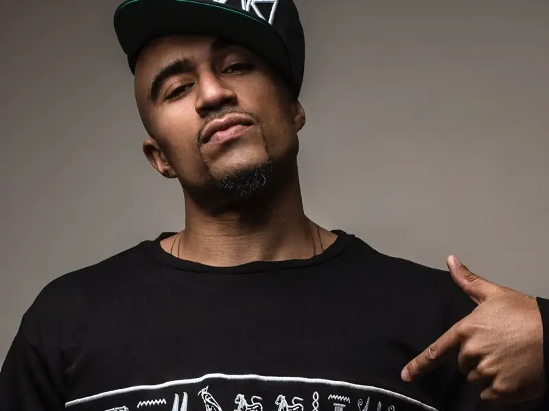 Stylish man in black cap and sweatshirt with Egyptian hieroglyphs, pointing downward—reflecting on failed relationships, financial stress, and sexual compatibility issues in 2025.