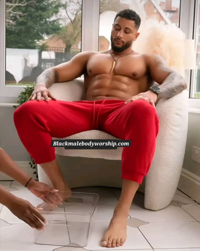 handsome Black man in red sweat pants gets his beautiful bare feet soaked, cleaned, and pedicured while relaxing indoors. showcasing Black men's foot grooming rituals as his feet are being worshipped 