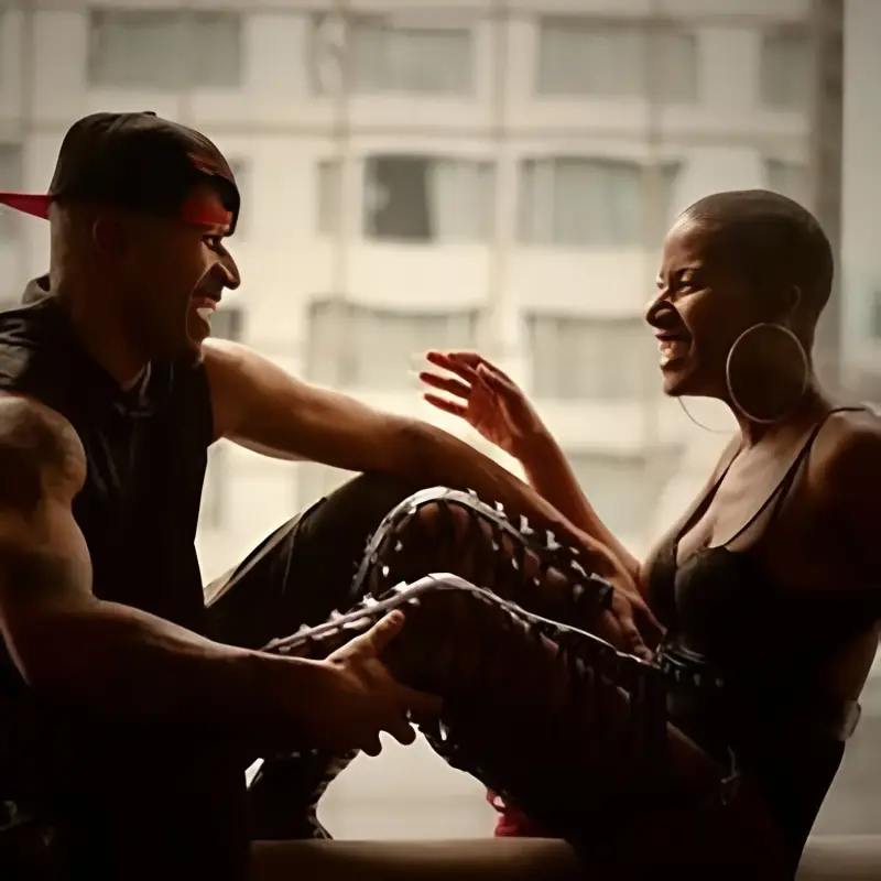 Smiling man in cap and muscular physique interacts with vibrant woman wearing earrings and lace-up boots, indoor setting—showcasing fetish and kink compatibility in modern relationships.