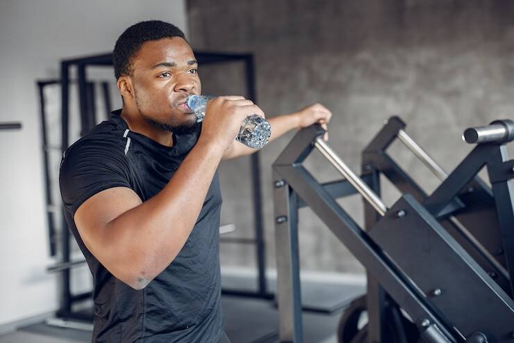 Black man in gym drinking water after workout, reflecting post-exercise body confidence and mental clarity