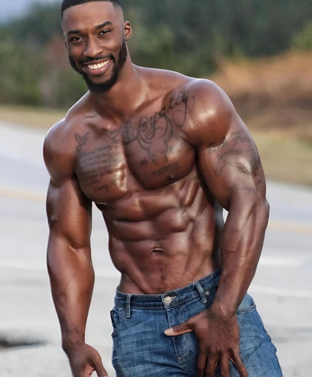 A dark-skinned Black male model poses shirtless, flaunting his muscular body and sculpted torso. His tattoos and confident smile enhance his dominant, alpha-male presence.