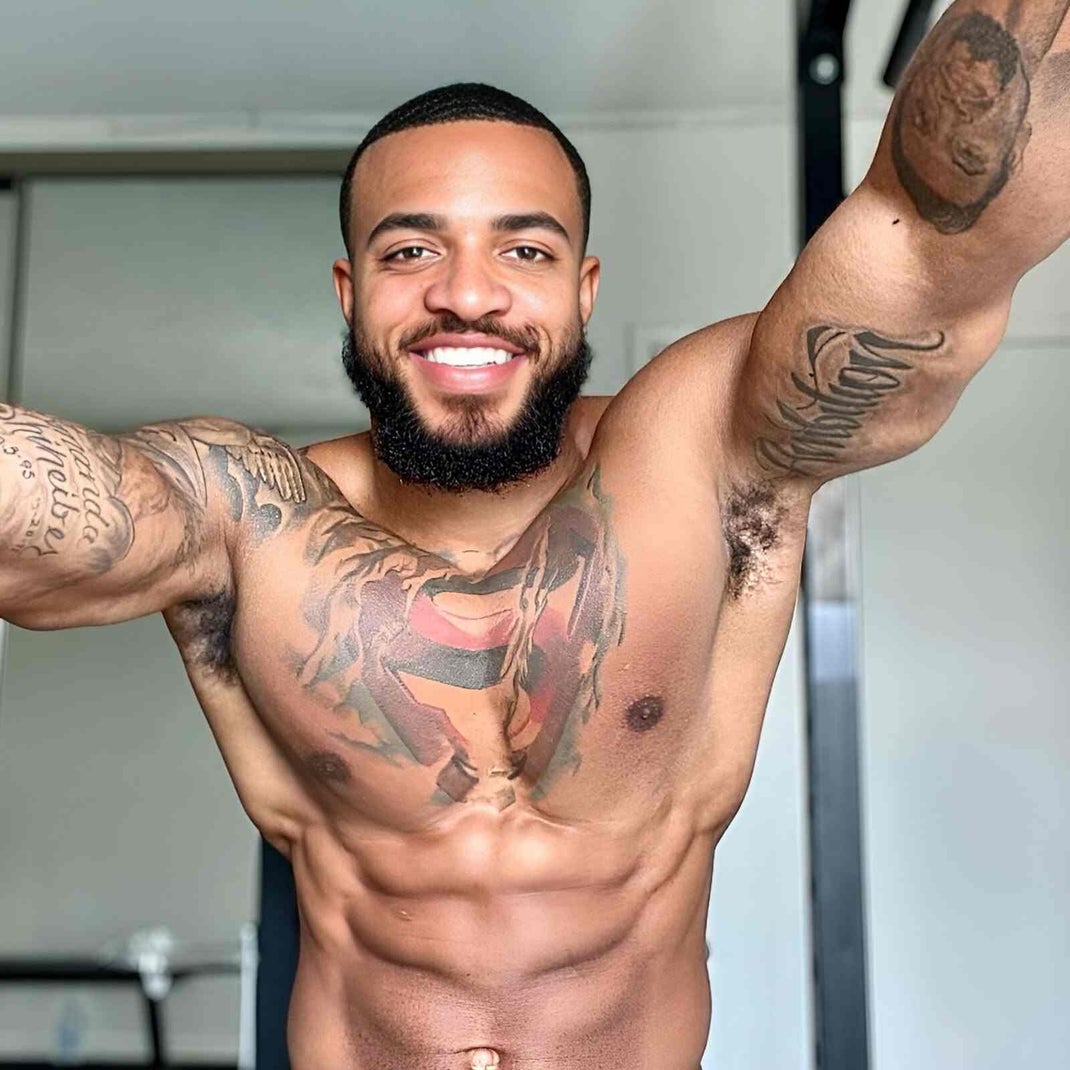 Smiling, muscular Black man with tattoos. Fitness motivation, showing defined abs and upper body strength.