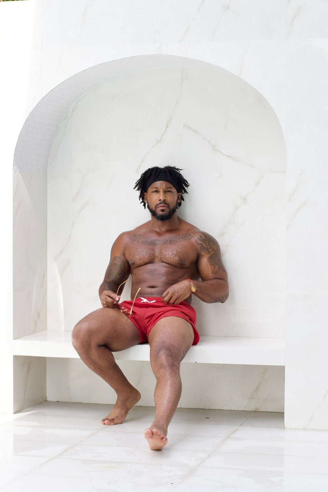 Tattooed man in red swim trunks posing to display his fit body and smooth, well-groomed feet, illustrating men’s foot health and preventing rough uncle feet.