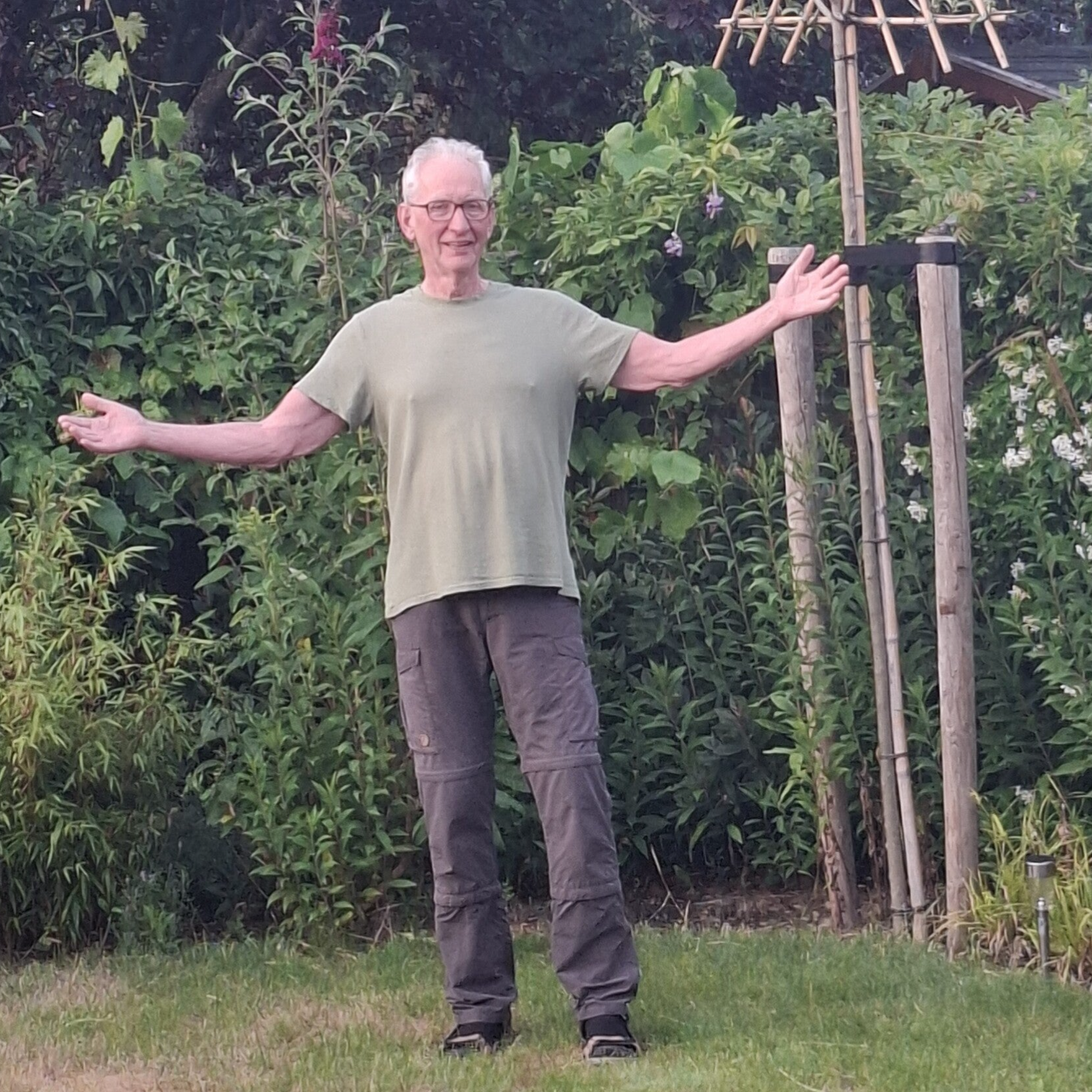 Marchal oefent Tai Chi Tao Qigong met open armen in een groene tuin.