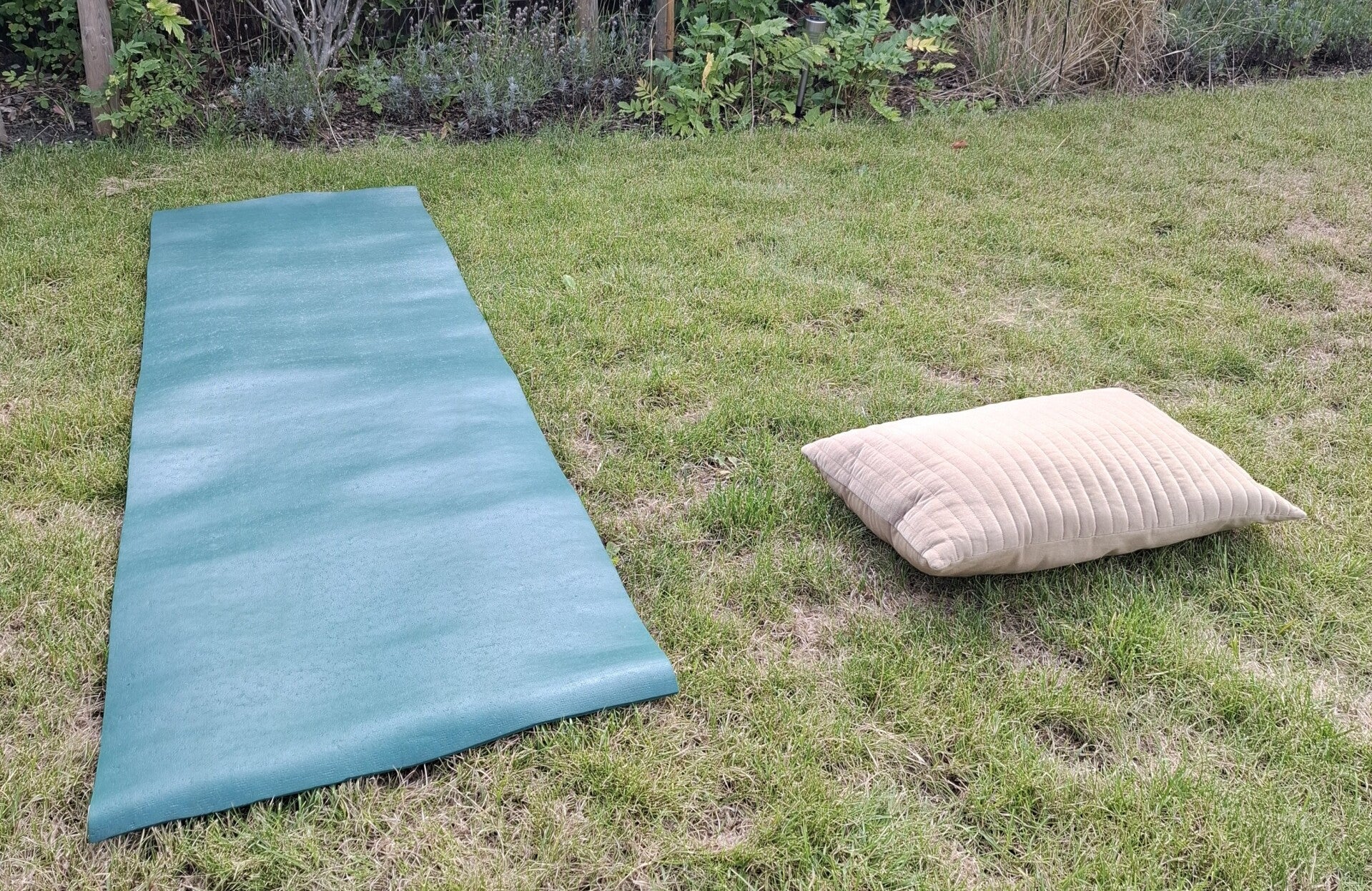 Lege yogamat en kussen in een groene tuin in Alkmaar, klaar voor een rustig moment.