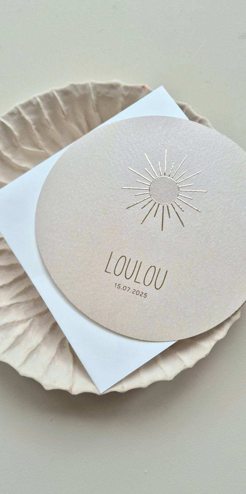 Dit net niet ronde geboortekaartje heeft een prachtig zonnetje op de voorzijde en heeft een unisex kleur zand/grijs. Zowel de voornaam als de zon worden gedrukt in goud foliedruk.  Door zijn bijzondere vorm past hij helemaal in de trend anno 2022. Zowel d