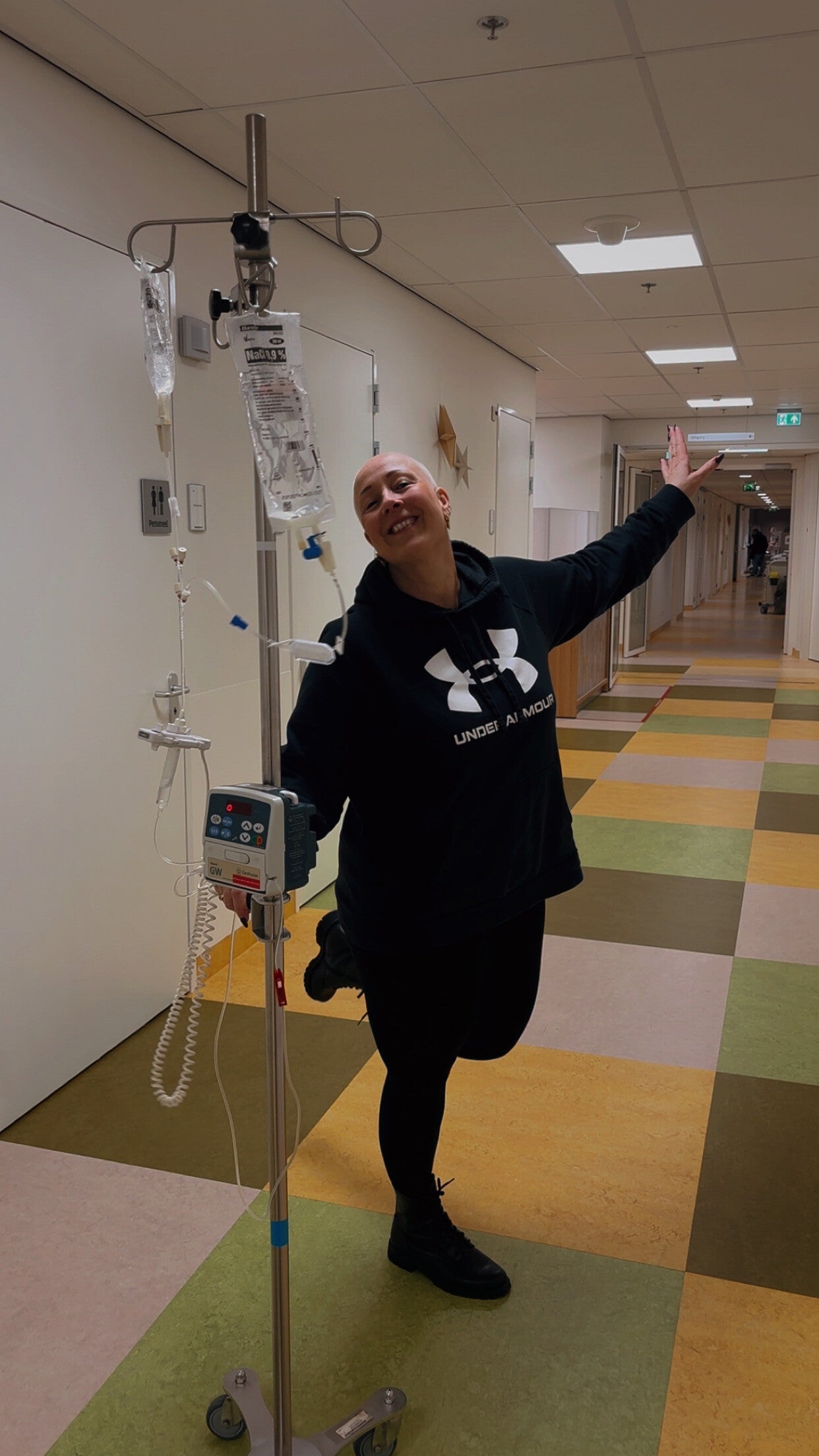Tamara van My Shitty Titty Life lachend in een ziekenhuisgang tijdens haar borstkankerbehandeling.