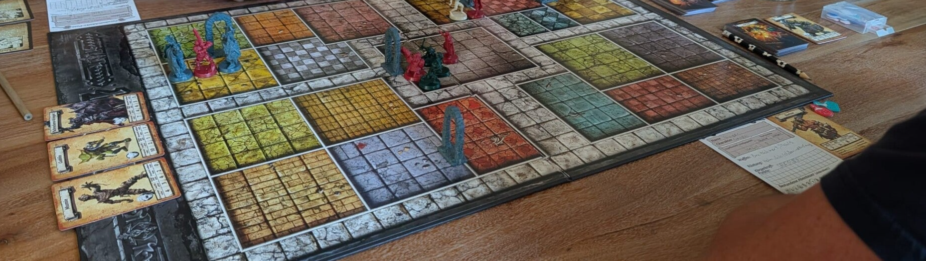 Spieleabend mit dem Brettspiel HeroQuest: Figuren, Heldenkarten und Charakterpässe auf einem Holztisch