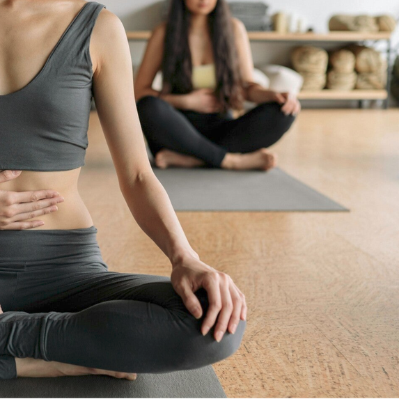 zwei Frauen in einem Yogastudio mit ihren rechten Händen auf dem Bauch, die Linke liegt auf dem Knie