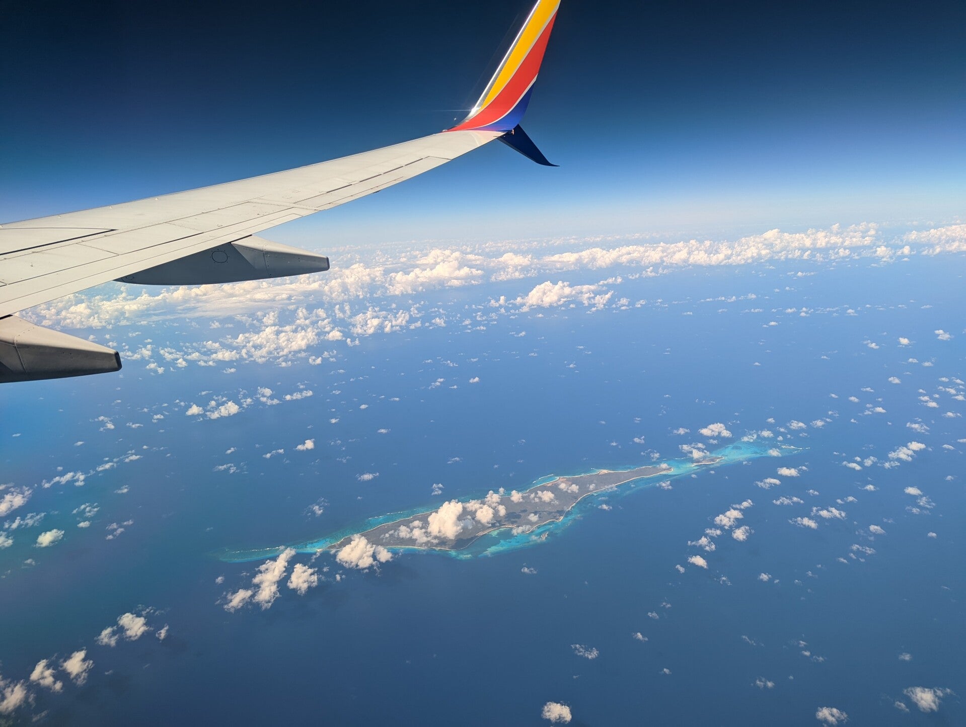 Airplane wing over skyview of ocean.