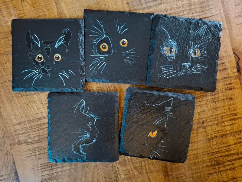 "Set van vijf handbeschilderde leistenen onderzetters met zwarte schaduwpoezen in verschillende houdingen."