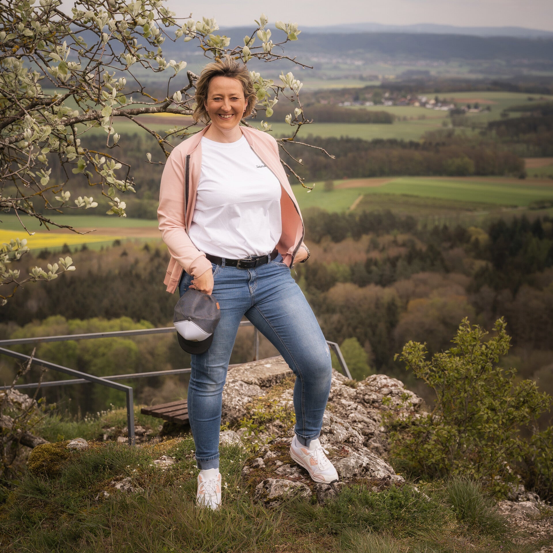 Eine Frau posiert vor einer Felswand und trägt ein senfgelbes T-Shirt mit einem auffälligen Brusttaschen-Design, kombiniert mit einer engen Jeans und einer blauen Beanie. Der Look vermittelt Outdoor-Abenteuer und Freizeitmode.
