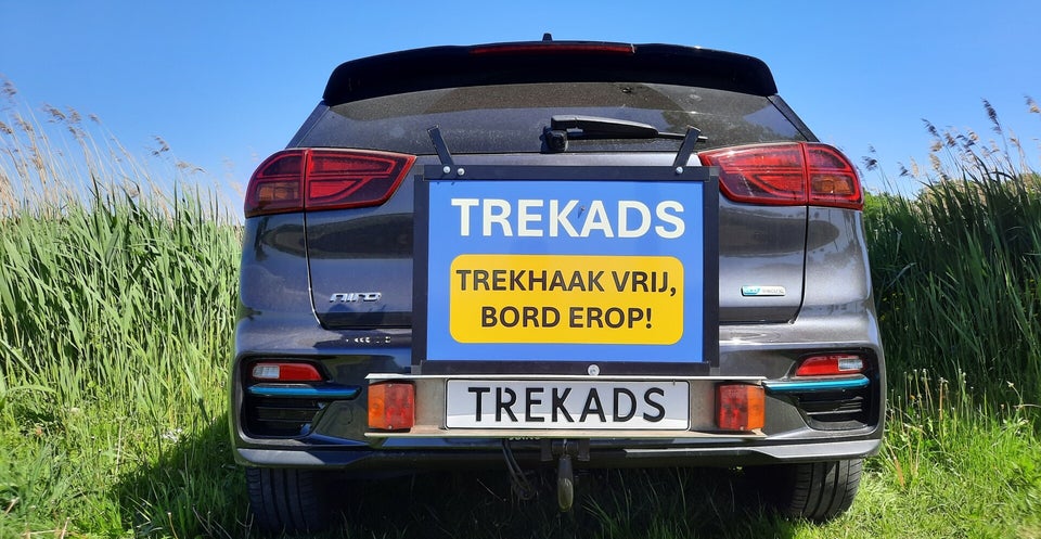 TrekAds reclamebord op trekhaak van auto, auto staat geparkeerd in grasveld.