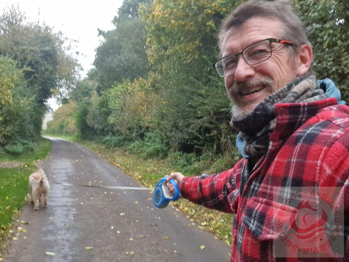 Dog walker walking a labradoodle along a country road in the Cotswolds