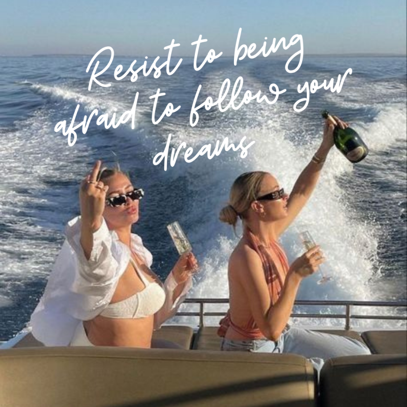 Two blond women on a spead boat drinking champagne.  One of them has her middle finger in the aire.  Resist2it.com