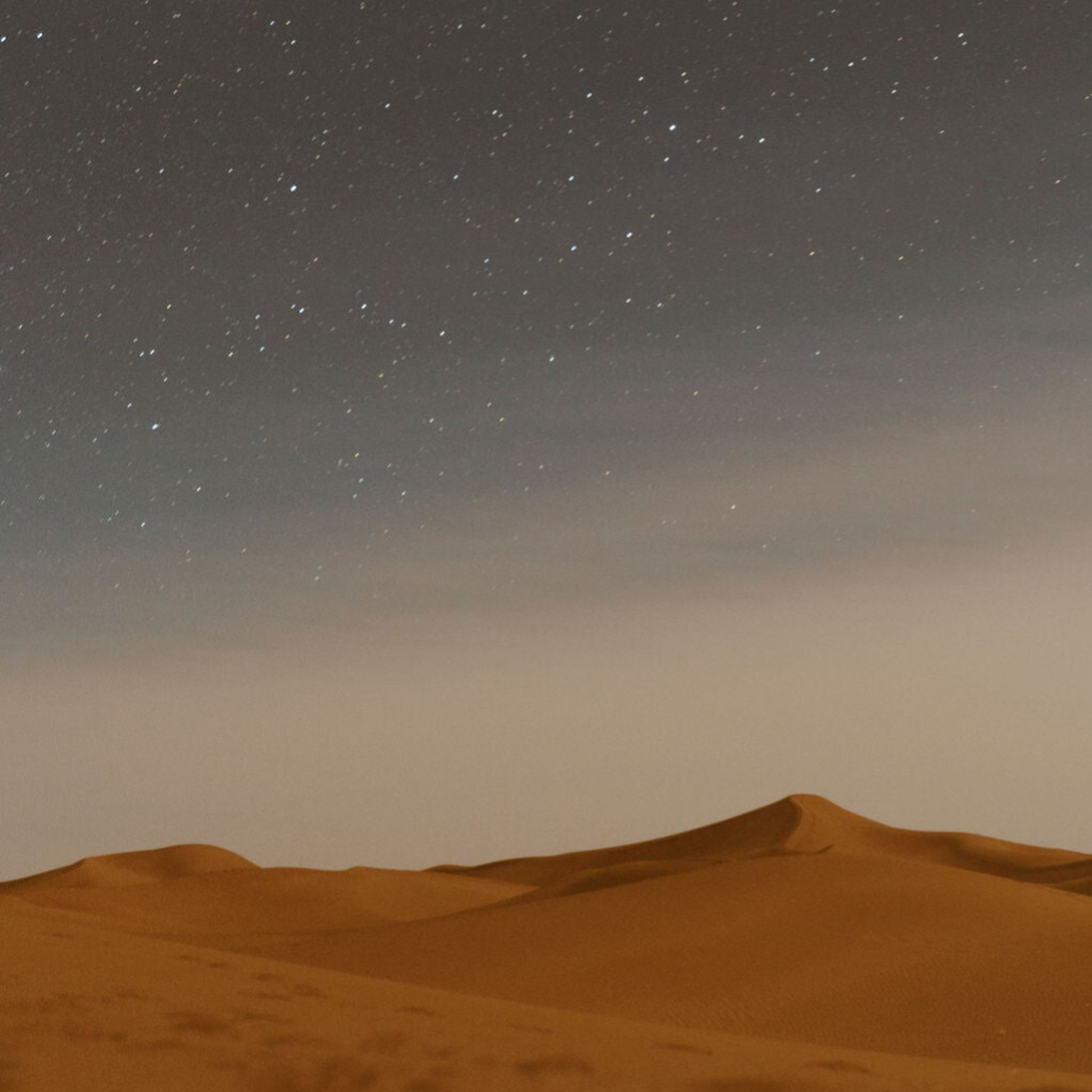 Sahara Desert dune at sunset with starry night sky.