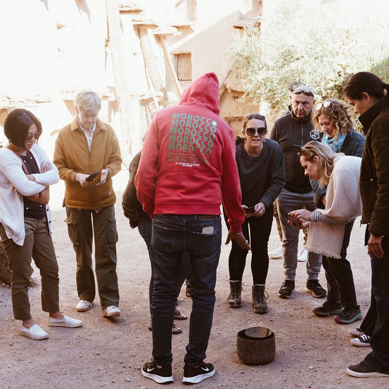 A retreat group gathered around a local Moroccan guide, learning about traditional cultural practices and historical customs during an immersive group experience.