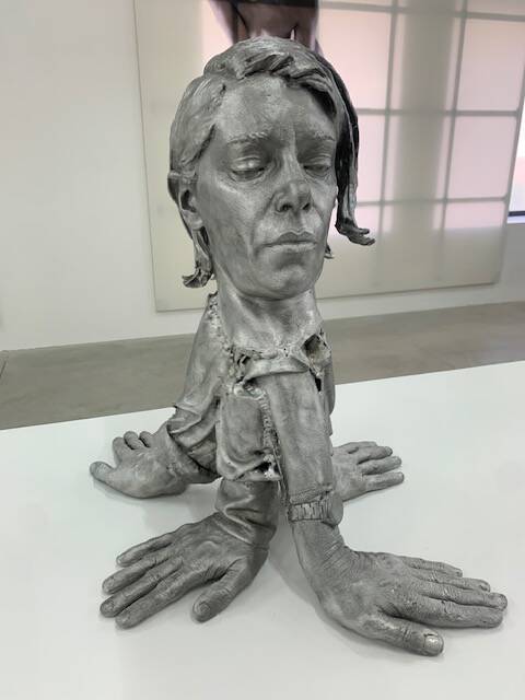 Photo 2 : sculpture en aluminium représentant le visage de l’artiste avec, sous le cou, 4 avant-bras et mains.