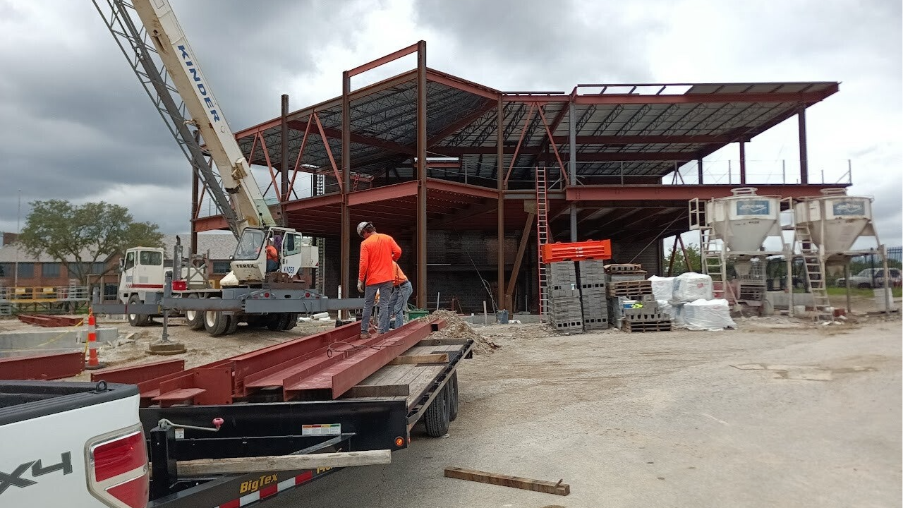 Structural steel fabrication and on-site erection of a commercial steel building frame using crane-lifted beams and welded connections.