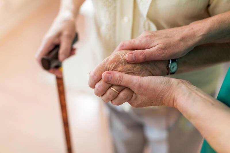 senior avec une canne soutenue par une main