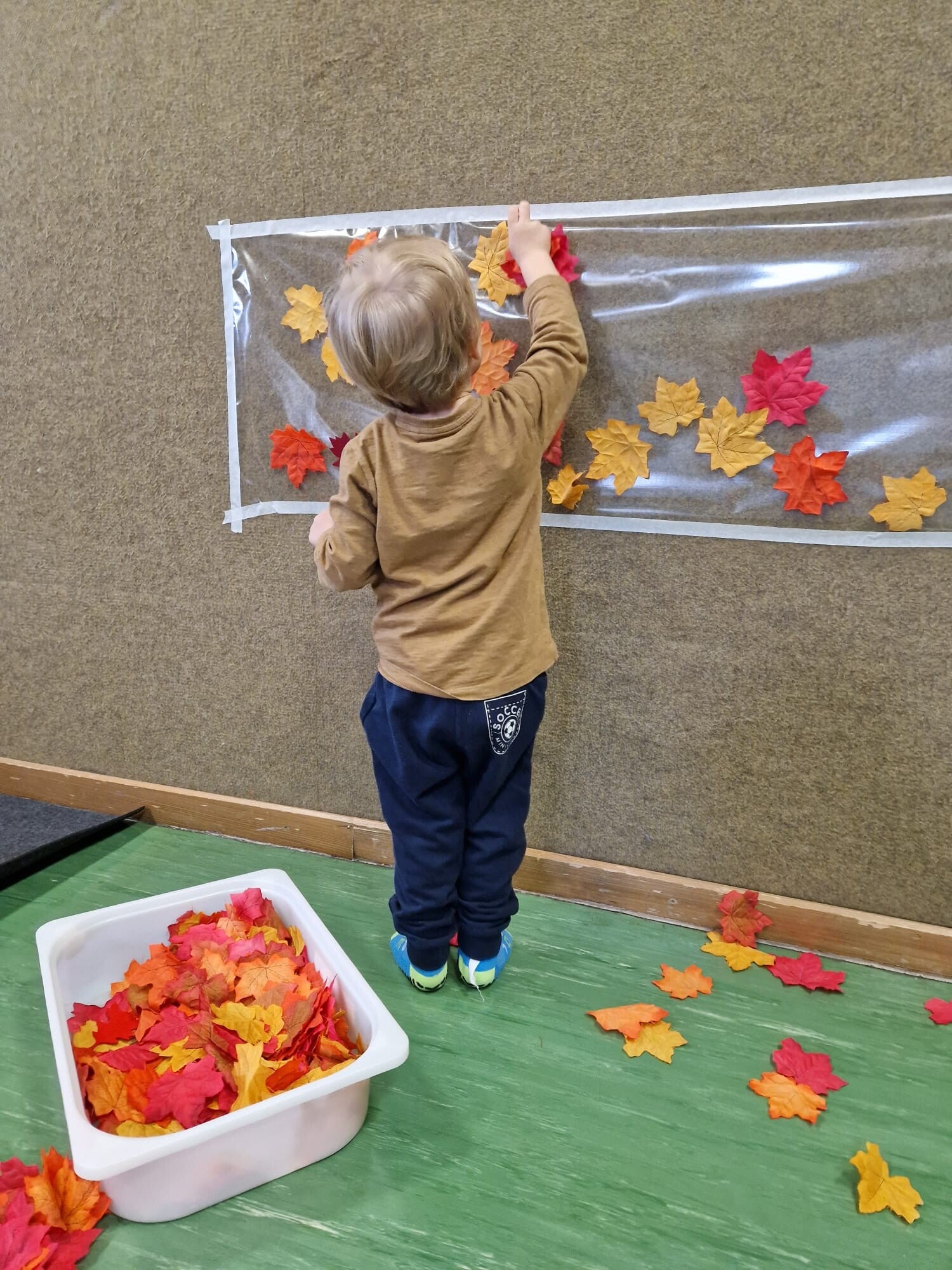 Kind gestaltet mit bunten Herbstblättern an einer transparenten Fläche.