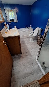 Spacious bathroom interior with vibrant royal blue walls, light grey wood-look flooring, a white bathtub, and a wood grain vanity.