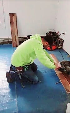 Worker using circular saw to cut wood during flooring or carpentry project.