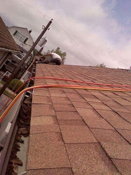 Worker on shingled roof with colored cables running toward roof peak.