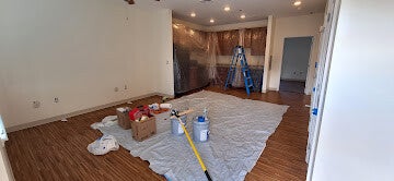 Room prepared for painting with drop cloth, paint cans, roller, and ladder.