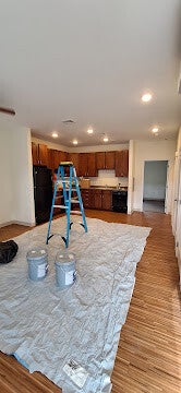 Professional kitchen renovation project featuring dark wood cabinets, black appliances, and protective floor covering during a home remodel.