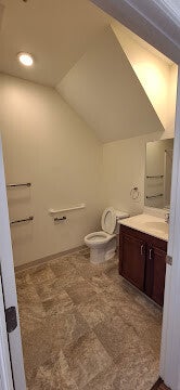 mall functional bathroom with a sloped ceiling, dark wood vanity, neutral tile flooring, and ADA-compliant grab bars.