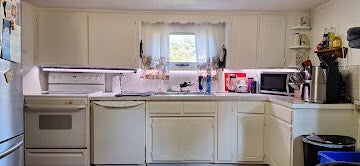 Bright cottage-style kitchen featuring white cabinets, a double-basin sink, and floral cafe curtains over a center window.