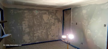 Room with patched drywall, work light, and painter’s tape preparing for painting.