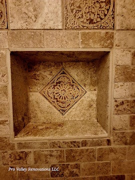 Close-up of a finished built-in travertine shower niche featuring a central diamond-pattern decorative accent tile, completed by Pro Valley Renovations LLC.