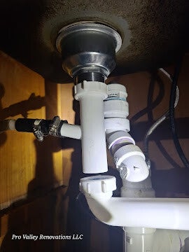 Close-up of a professional under-sink plumbing installation featuring white PVC P-trap pipes and drainage connections.
