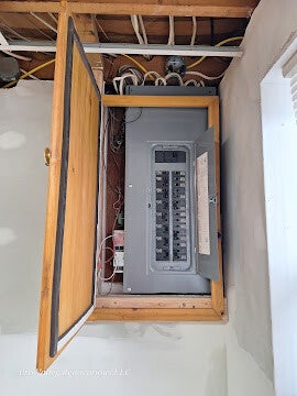 Residential electrical breaker panel installed inside wooden cabinet.
