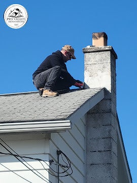 Worker performing roof and chimney maintenance on shingled roof.