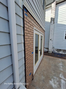 Exterior renovation showing transition between vinyl siding and brick veneer with double glass doors.