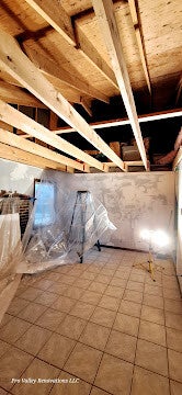 Renovation space with exposed ceiling beams, ladder, and work light.