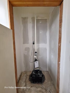 Sump pump system installed in unfinished utility room with patched drywall.