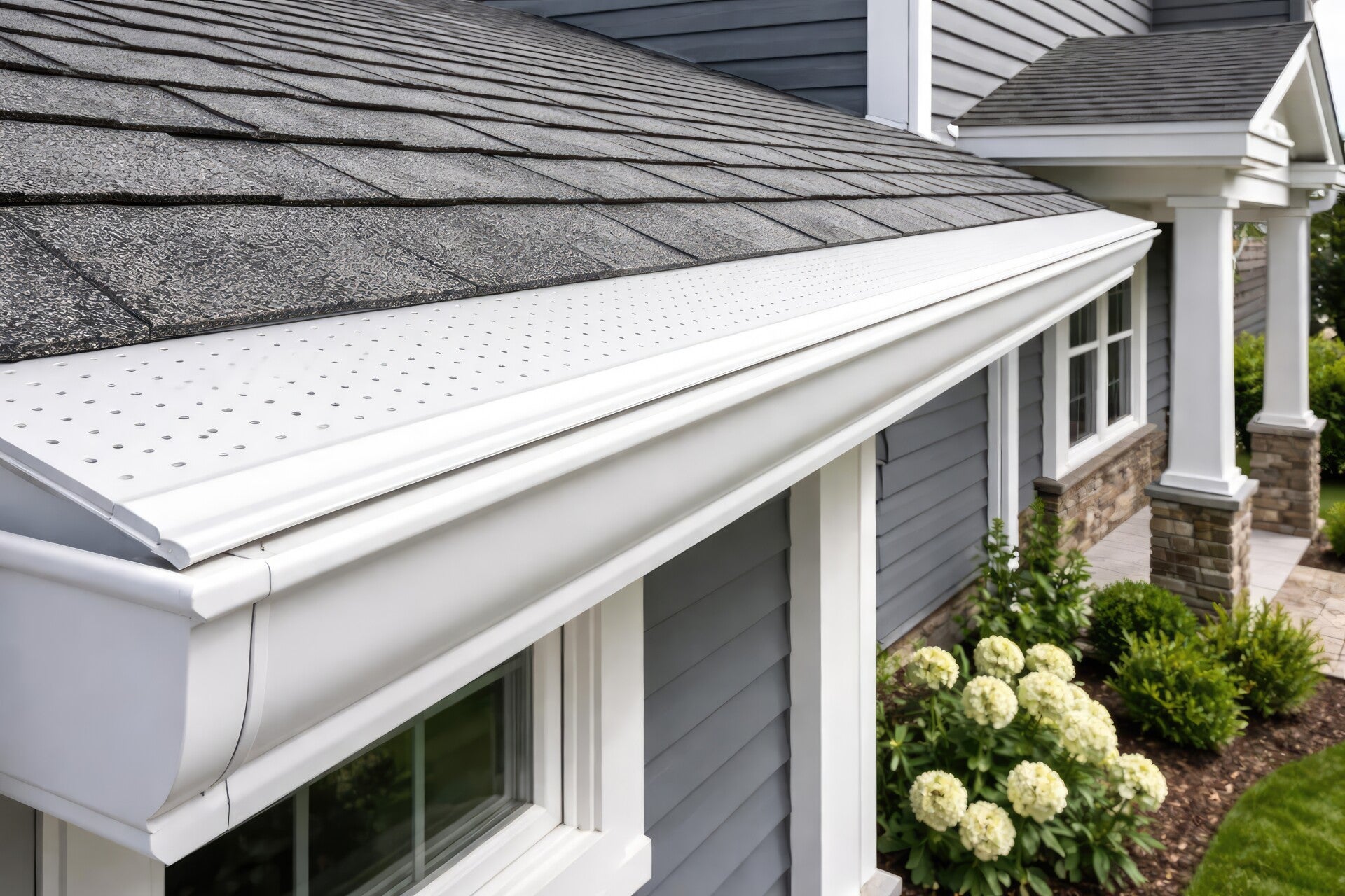 House roofline with gutter guard system and landscaped shrubs below.