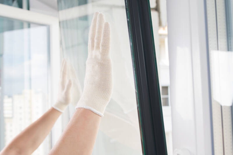 Hand cleaning interior glass window with cloth for streak-free shine in bright room.