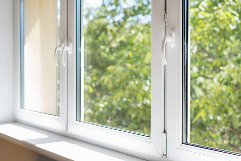 Clean modern home window with natural sunlight and green trees outside view. 