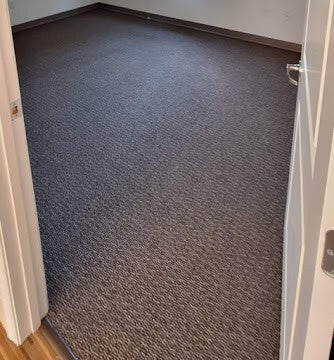 Empty interior room with dark carpet, light walls, and baseboard trim.
