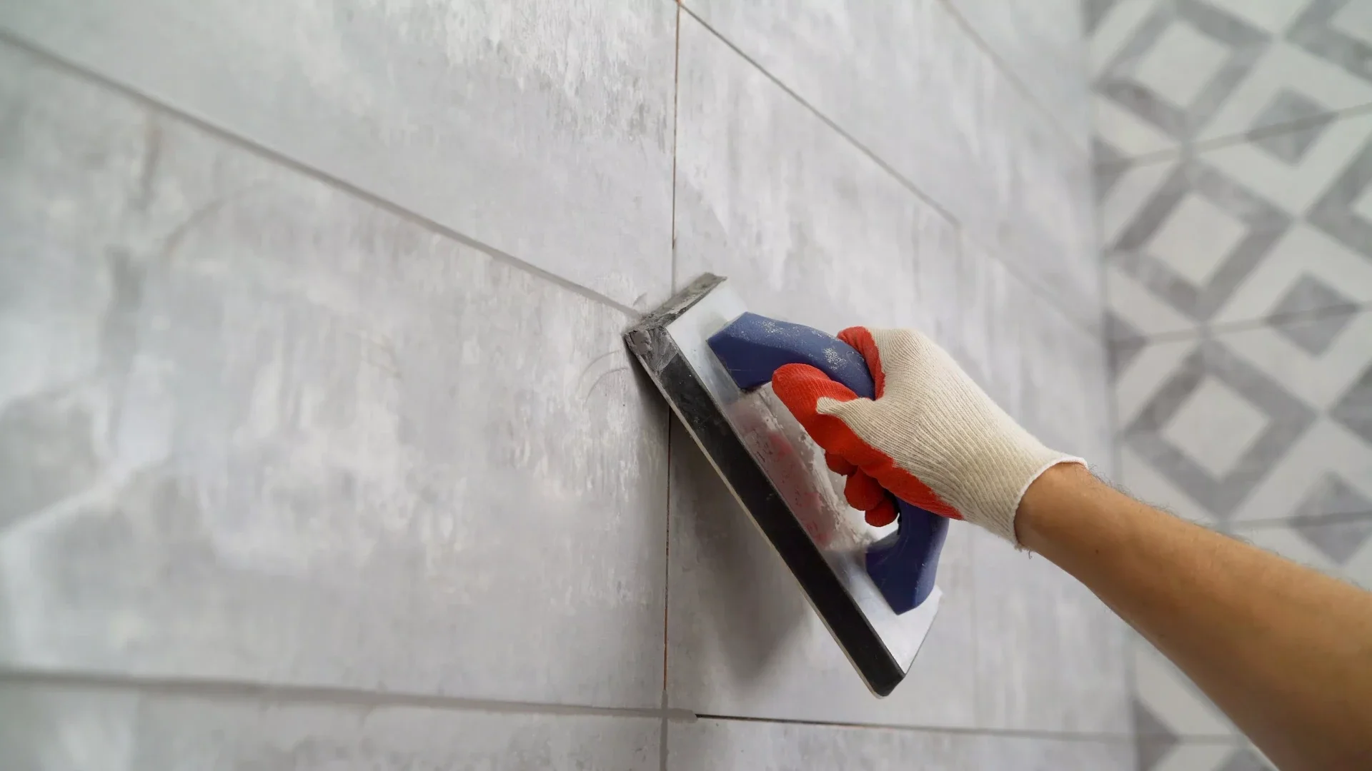 Worker applying grout between ceramic tiles using a grout float.