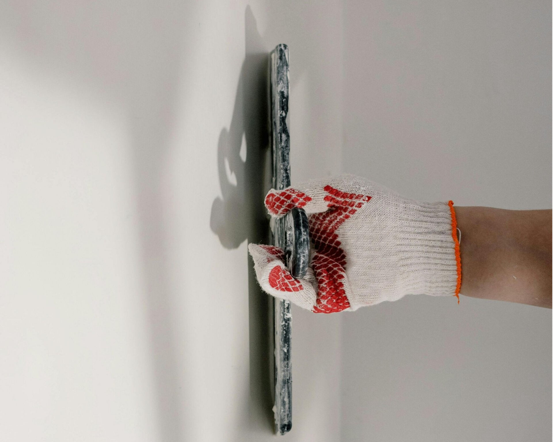 Worker applying plaster or joint compound to wall using a metal trowel.