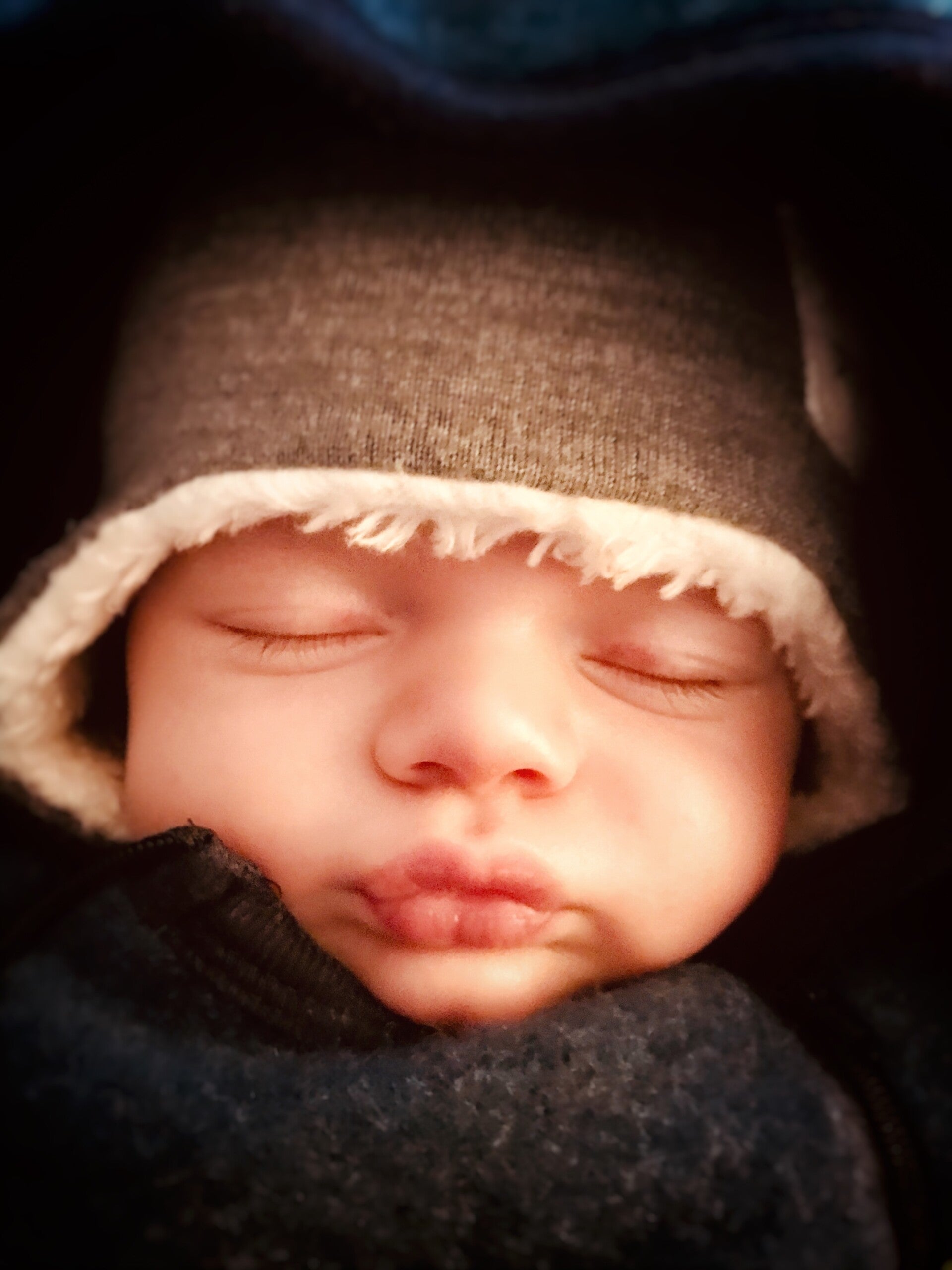 Der Kopf eines schlafenden Babys mit Schmollmund ist zu sehen. Das Baby trägt eine graue Mütze mit weißem Innenfutter