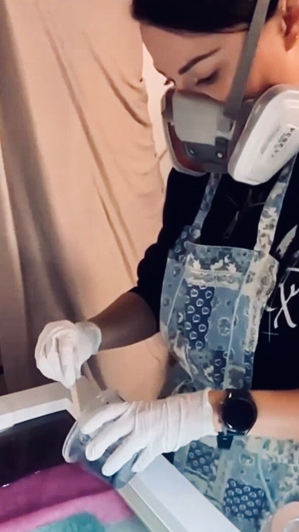 Künstlerin der Waldesruf Schmuckerei bei der Arbeit mit Epoxidharz: Trägt Atemschutzmaske und Nitrilhandschuhe zum sicheren Gießen von Schmuck mit Blumen in der Werkstatt.